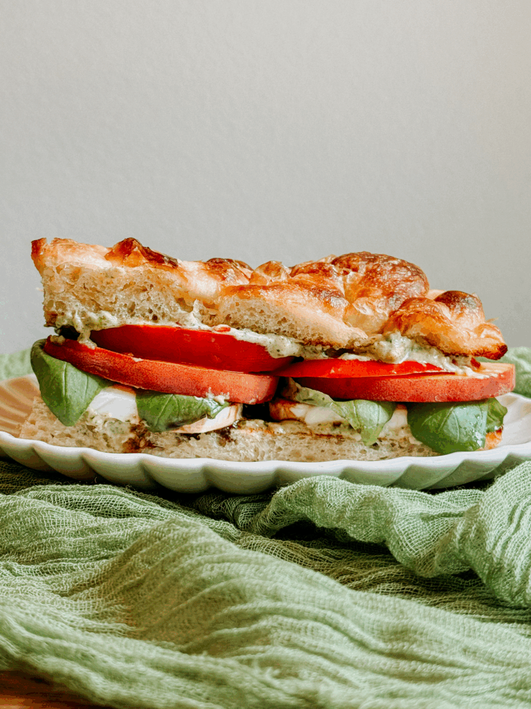 Side view of a peach caprese sandwich layered with fresh tomato, basil, mozzarella, and pesto mayo on toasted focaccia