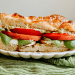 Close-up of peach caprese sandwich with visible layers of tomato, basil, mozzarella, and pesto mayo on toasted focaccia