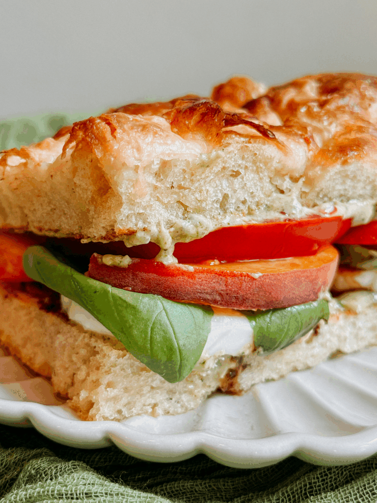 Close-up of Peach Caprese Sandwich on a plate, showing thick peach and tomato slices with basil and mozzarella.
