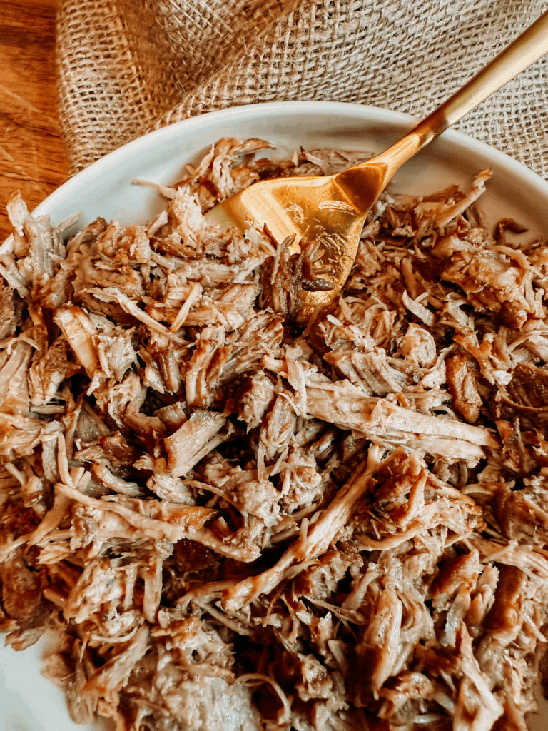 Close-up of tender shredded pulled pork on a white plate with a gold serving fork