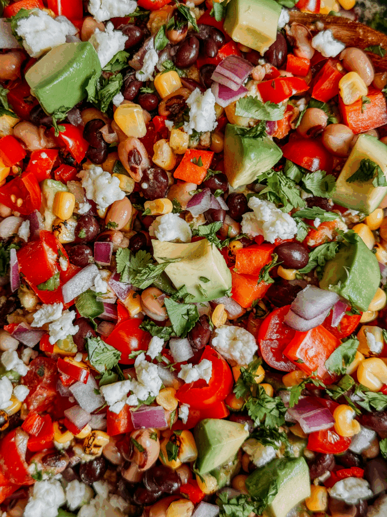 Overhead close-up of Cowboy Caviar bean salad with avocado, black beans, corn, peppers, onion, cilantro, and cotija cheese.