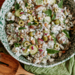 Tzatziki potato salad in a green speckled bowl with cucumbers, olives, chickpeas, and fresh herbs.