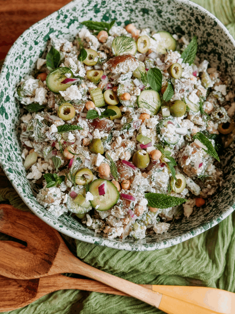 Tzatziki potato salad in a green speckled bowl with cucumbers, olives, chickpeas, and fresh herbs.