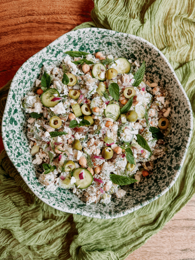 Tzatziki potato salad in a speckled green bowl with cucumbers, olives, chickpeas, and herbs.