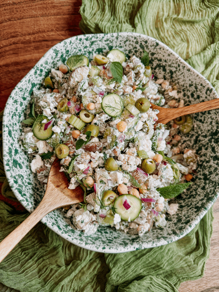Tzatziki potato salad in a serving bowl with wooden spoons.