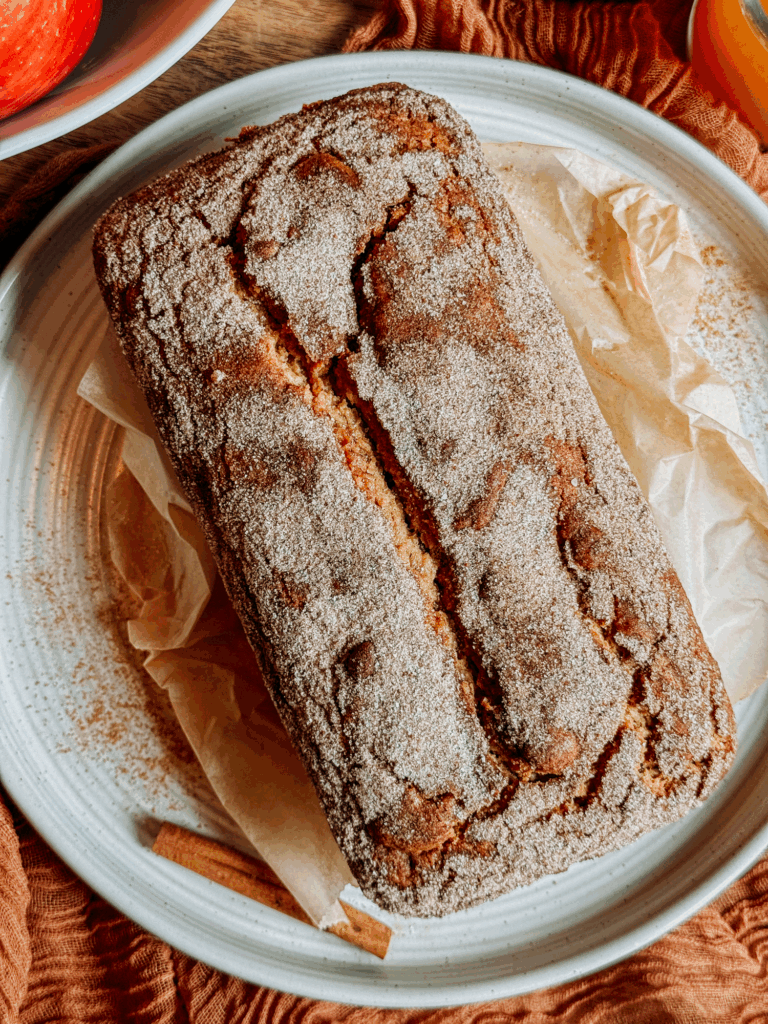 Whole apple cider donut bread with a cinnamon-sugar crust on a parchment-lined plate.