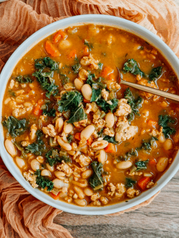 Close-up bowl of Turkey Pumpkin White Bean Chili with kale, carrots, celery, and cannellini beans in a warmly spiced pumpkin broth.