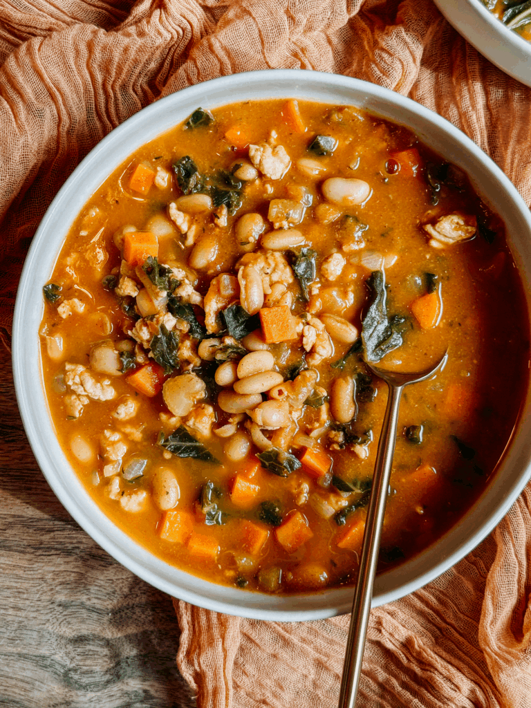 Close-up of a bowl of Turkey Pumpkin White Bean Chili with carrots, kale, cannellini beans, and ground turkey in a warm pumpkin broth.