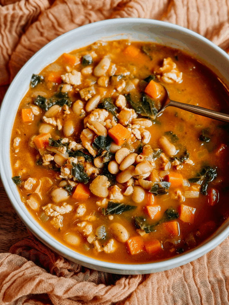 Macro close-up of Turkey Pumpkin White Bean Chili showing tender white beans, turkey, carrots, and kale in a creamy pumpkin broth.