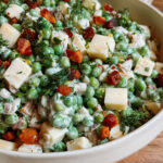 Herby pea salad with Gruyère and crispy pancetta in a white serving bowl