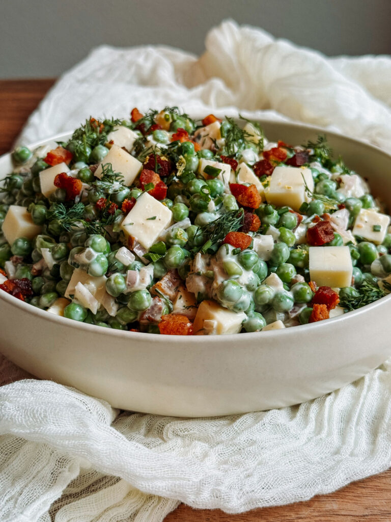 Herby pea salad with Gruyère and crispy pancetta in a white serving bowl