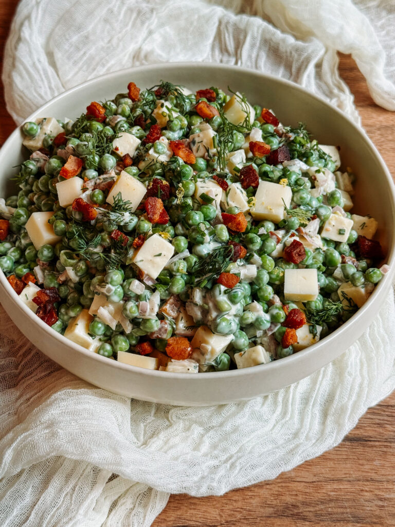 Herby pea salad with Gruyère and crispy pancetta in a white serving bowl