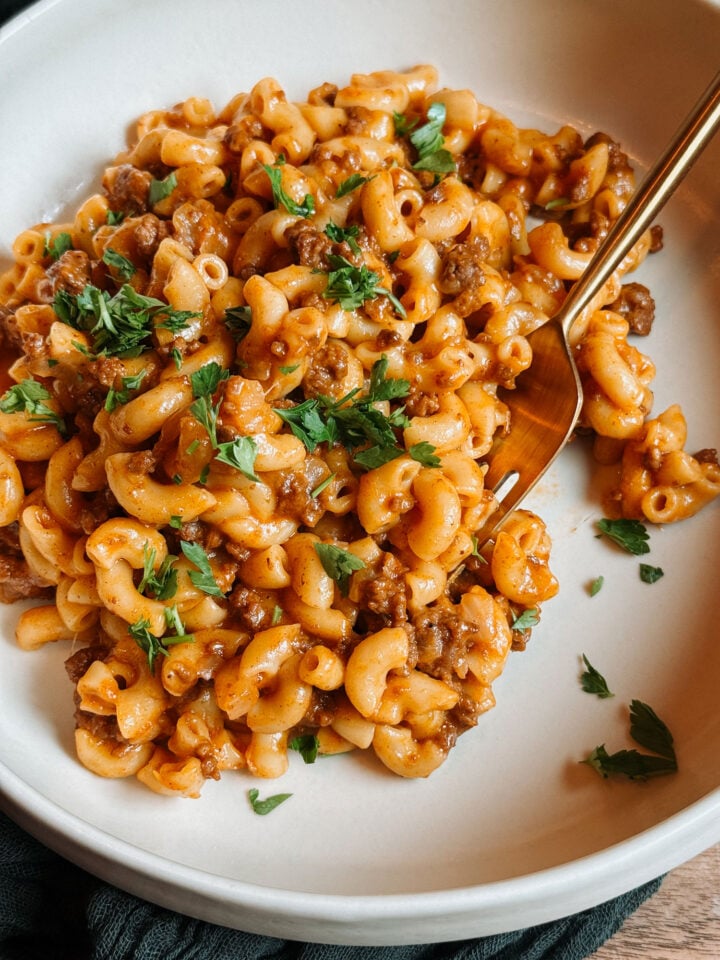 Close-up of creamy Instant Pot Hamburger Helper with elbow macaroni, ground beef, cheddar sauce, and parsley in a white bowl.